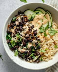 a white bowl filled with rice, black beans and cucumber garnish