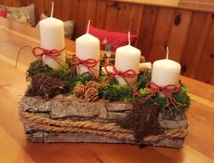 some white candles are sitting on a piece of driftwood with moss and pine cones