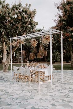 an outdoor dining set up with white chairs and flowers hanging from the ceiling over it