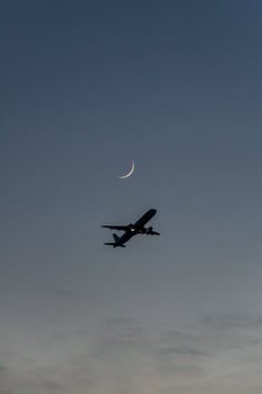 an airplane is flying in the sky at dusk with a half moon visible above it