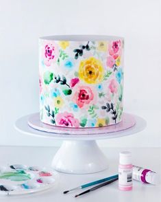 a white cake with colorful flowers painted on it and paintbrushes next to it