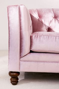 a pink velvet chair with wooden legs and buttoned back rests against a white wall