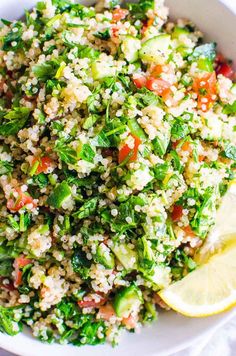 a white bowl filled with rice and veggies next to a slice of lemon