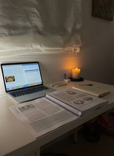 an open laptop computer sitting on top of a desk next to a book and candle