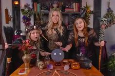 three women dressed up as witches posing in front of a table with decorations on it