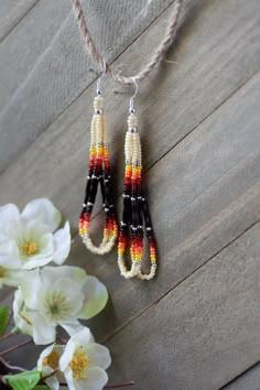 three beaded earrings hanging from a string on top of a wooden table next to flowers