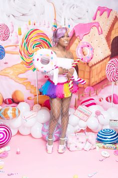 a woman standing in front of a candy land backdrop with balloons, candies and lollipops