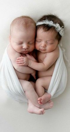 two babies are cuddling together wrapped in white cloths and laying on top of each other