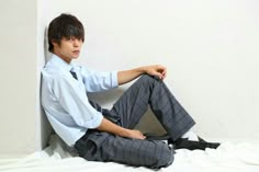 a young man sitting on top of a bed next to a white wall with his legs crossed