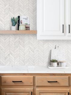 a white kitchen with wooden cabinets and herringbone tile on the backsplash wall