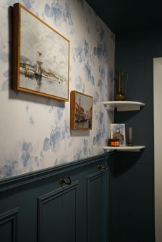 a room with blue and white wallpaper, two pictures hanging on the wall next to bookshelves