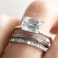 a woman's hand holding two rings with an emerald and diamond set on it