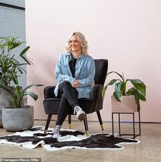 a woman sitting in a chair with her legs crossed on a cowhide rug next to potted plants