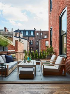 an outdoor living area with couches, tables and chairs on the balcony overlooking brick buildings