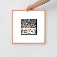 a person holding up a framed art print with an image of a house in the woods