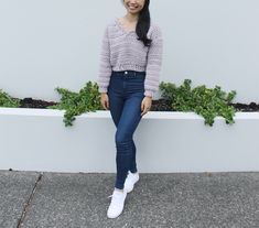 a woman standing next to a white wall with plants in the corner and smiling at the camera