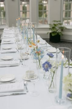 a long table is set with white plates and silverware, blue candles and flowers