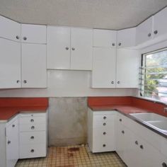 an empty kitchen with white cabinets and red counter tops