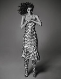 a woman with long hair standing in front of a gray background wearing a floral dress