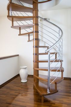 a wooden spiral staircase in an empty room with a vase on the floor next to it