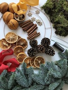 pine cones, oranges and cinnamon sticks are arranged on a white table with evergreen branches