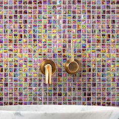 two gold faucets in front of a colorful mosaic tile backsplashe