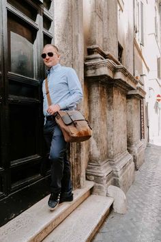 a man is standing on the steps in front of an old building wearing sunglasses and a blue shirt