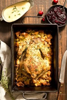 a roasting pan filled with meat and vegetables on top of a wooden table next to utensils