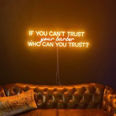 a brown leather couch sitting under a neon sign that says if you can't trust your danger who can you trust?