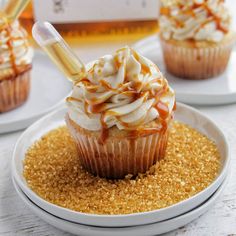 two cupcakes with caramel drizzle on top, one is topped with whipped cream and the other has gold sprinkles