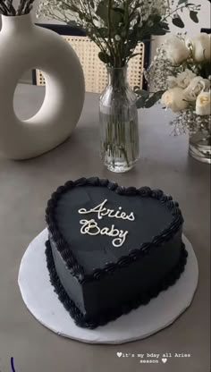 a black heart shaped cake sitting on top of a table next to vases and flowers