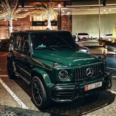 a green mercedes benz g class parked in front of a building with christmas decorations on the windows