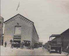 an old black and white photo of horses pulling carriages in front of a brick building