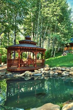 a gazebo sitting on top of a lush green field next to a lake and forest