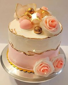 a three tiered cake decorated with pink roses and gold accents on a silver platter