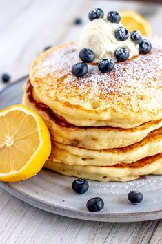 a stack of pancakes with blueberries and butter on a plate next to lemon wedges