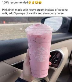 a person holding up a pink drink in their hand while sitting in the drivers seat of a car