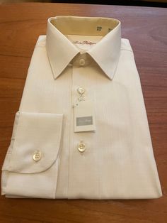 Sophisticated unworn 80s vintage shirt in original packaging in lemon blush polyester cotton mix by Louis Philippe.  Details: straight collar, long sleeves, barrel cuffs, regular fit.  55% Polyester 45% Cotton  Size M Chest 40" Collar 15" Cream Spread Collar Shirt For Spring, Classic Beige Collared Shirt, Classic Beige Shirt With Button Cuffs, Elegant Cream Shirt For Office, Elegant Beige Business Tops, Elegant Beige Business Top, Elegant Beige Tops For Business, Formal Cream Shirt With Button Cuffs, Cream Long Sleeve Shirt With Button Cuffs