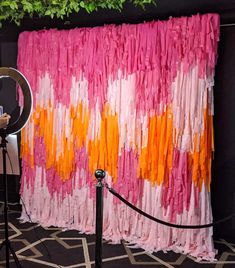 a pink, orange and white curtain is hanging on the wall next to a tripod