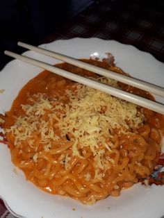 chopsticks resting on a plate of noodles with sauce and parmesan cheese