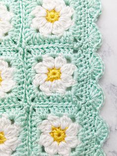 a crocheted granny granny blanket with white and yellow flowers on the center, sitting on a marble surface