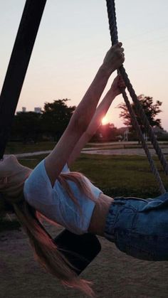 a woman hanging upside down on a rope swing at sunset or sunrise in the park