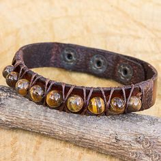 a brown leather bracelet with beads and metal fittings sits on a piece of wood