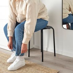 a woman sitting on a stool in front of a mirror tying her shoe laces