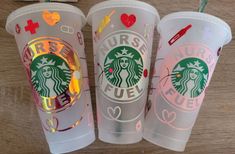 three starbucks cups sitting on top of a wooden table covered in stickers and hearts