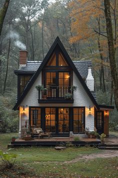 a small house in the woods with lots of windows and plants on the front porch