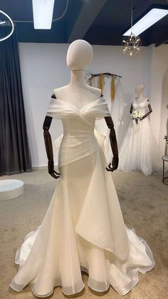 a white dress on display in a room with mannequins and other wedding gowns