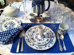 a blue and white place setting on a table with silver utensils, cups, and saucers