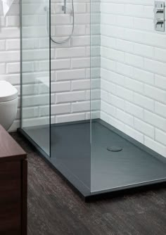 a bathroom with white brick walls and wooden floors, including a walk in shower next to a toilet