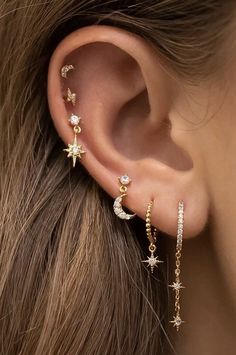 a woman's ear is shown with three stars and two moon charms on it